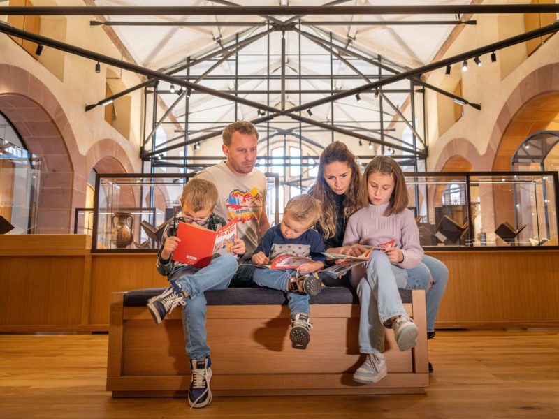 Famille assise sur un banc avec une brochure dans la salle d'exposition permanente de la Bibliothèque Humaniste